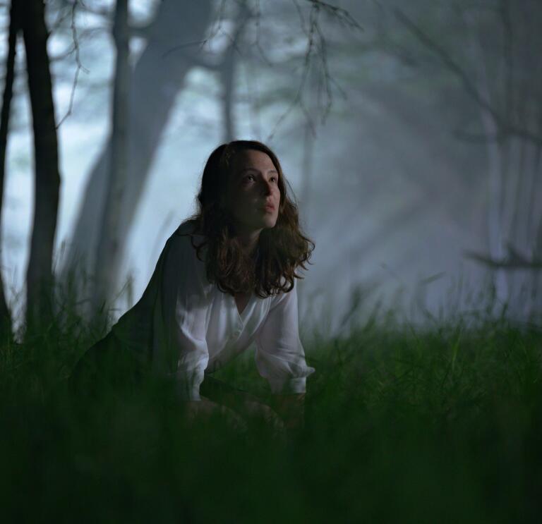 Une personne à genoux dans l'herbe dans une forêt sombre et effrayante la nuit