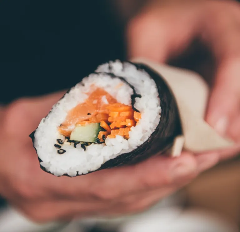 A hand holding a roll of sushi