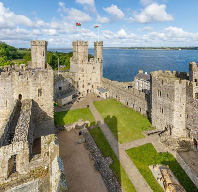 A picture of Caernarfon Castle, showing the inside lawn within the castle and the sea in the backdrop