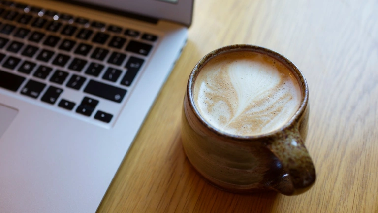 mug of coffee with open laptop computer showing keyboard