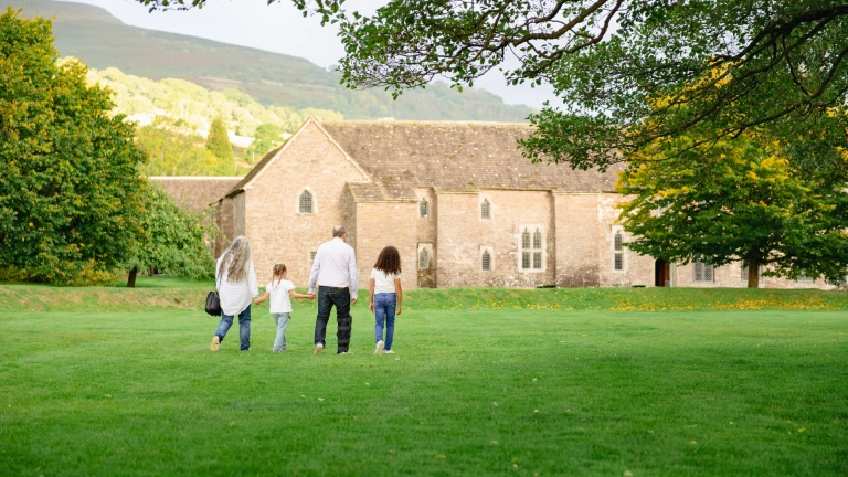 familia caminando en un campo hacia un edificio de piedra.