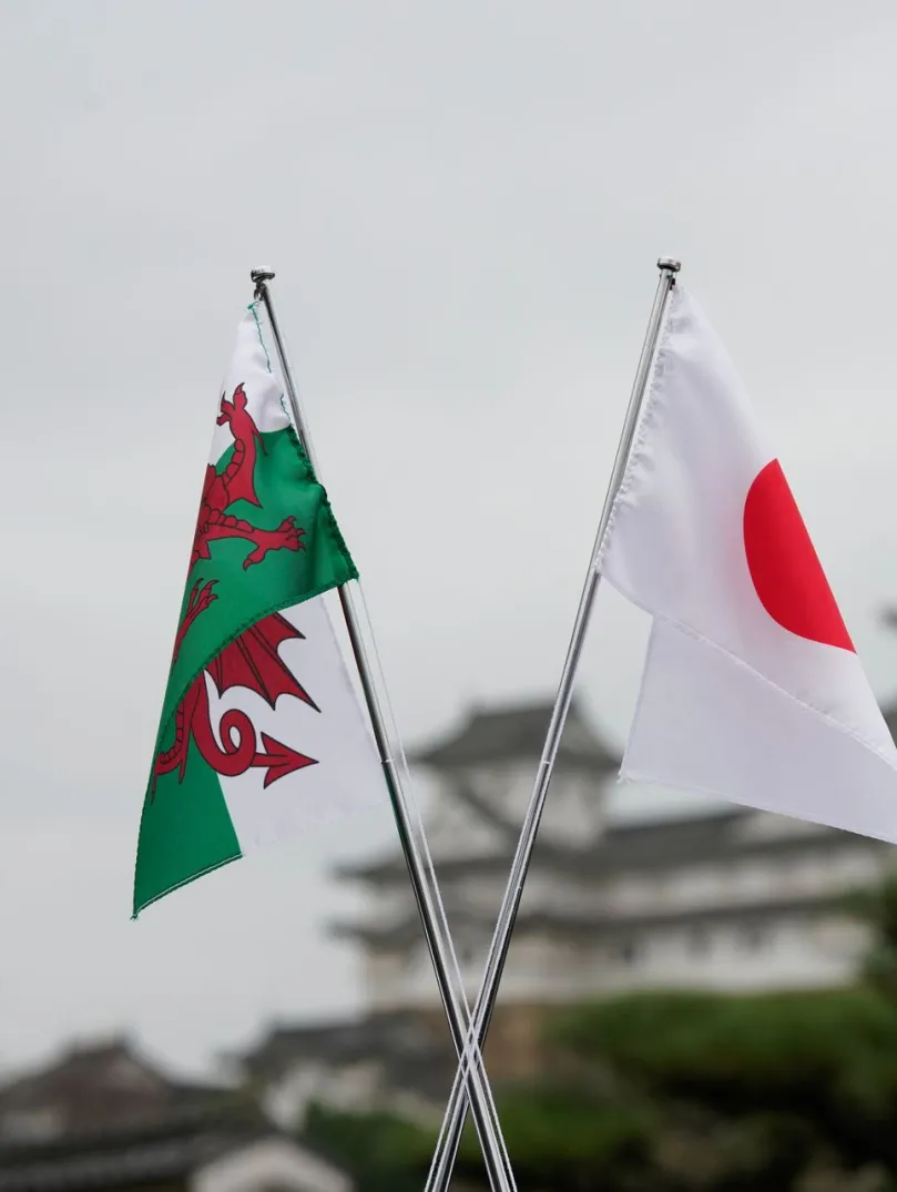 A Welsh flag and a Japanese flag shown in the foreground, with a Japanese castle in the background