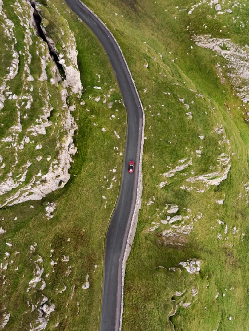Luftaufnahme eines Autos, das eine bergige Küstenstraße entlang fährt