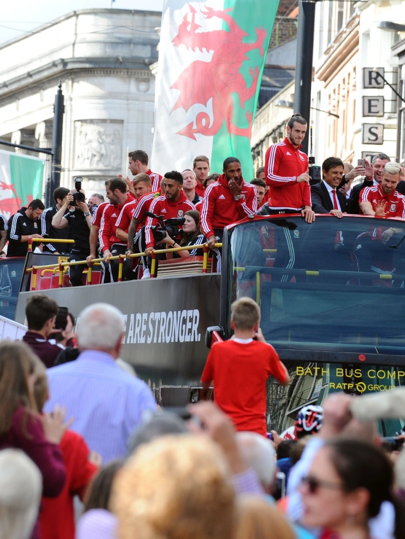 The Wales football team on top of their tour bus waving at crowds below.