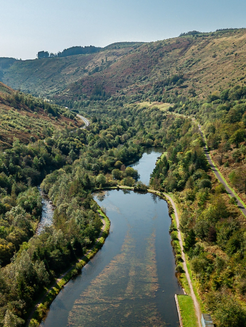 Drohnenaufnahme eines Sees, umgeben von grünen, bewaldeten Bergen.