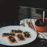 A plate with crackers garnished with laverbread (seaweed), with a red bowl also full of laverbread