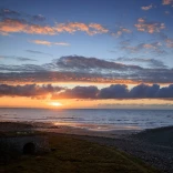 Una hermosa y colorida puesta de sol vista sobre una extensión de playa y costa.